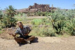 Image du Maroc Professionnelle de  Le paysage, formé par la kasbah Tifoultoute qui se dresse majestueusement sur un éperon rocheux qui domine la vallée de l'oued Ouarzazate, attire les touristes qui prennent le temps de s'arrêter pour prendre une photo. Précisément à cet endroit un charmeur de serpent tenant une vipère avec sa main droite tout en surveillant le mouvement du scorpion noir qu’il avait accroché à son cou avec sa main gauche pose aux touristes contre un billet avec derrière lui comme décor celui qui avait servit pour de grand films comme Lawrence d’Arabie et Jésus de Nazareth à quelque kilomètres de la ville de Ouarzazate au sud du Maroc le Samedi 23 Août 1997. (Photo / Abdeljalil Bounhar)
 